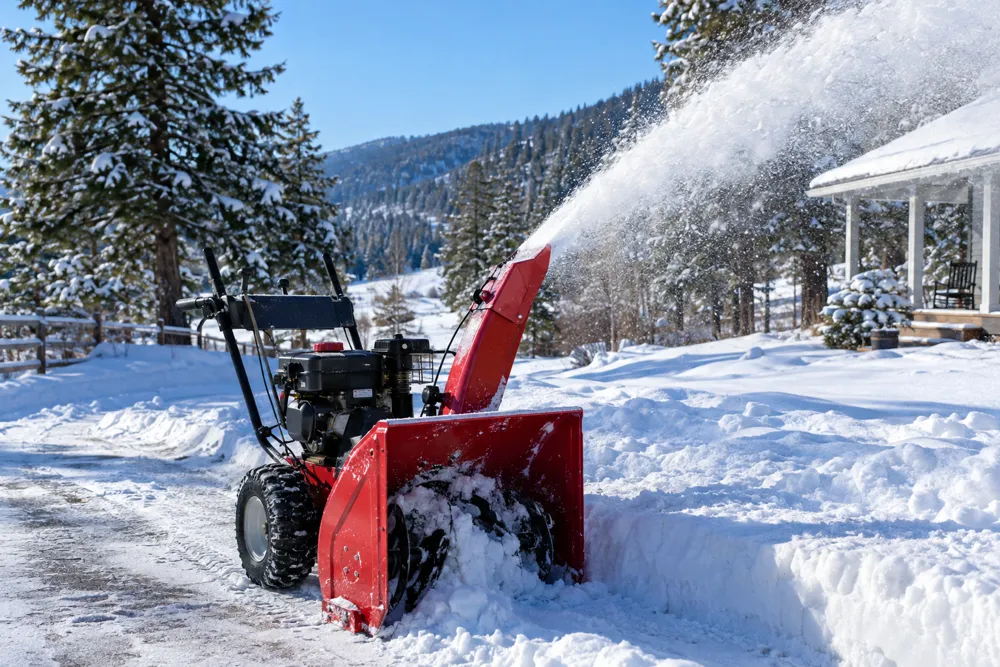 A red snowblower throwing snow off a rural driveway on a sunny winter morning